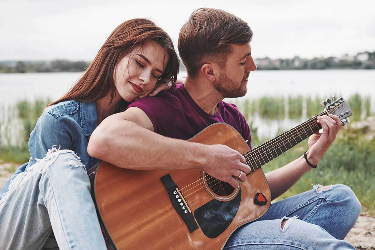 Feeling good. Man plays guitar for his girlfriend at beach on their picnic at daytime